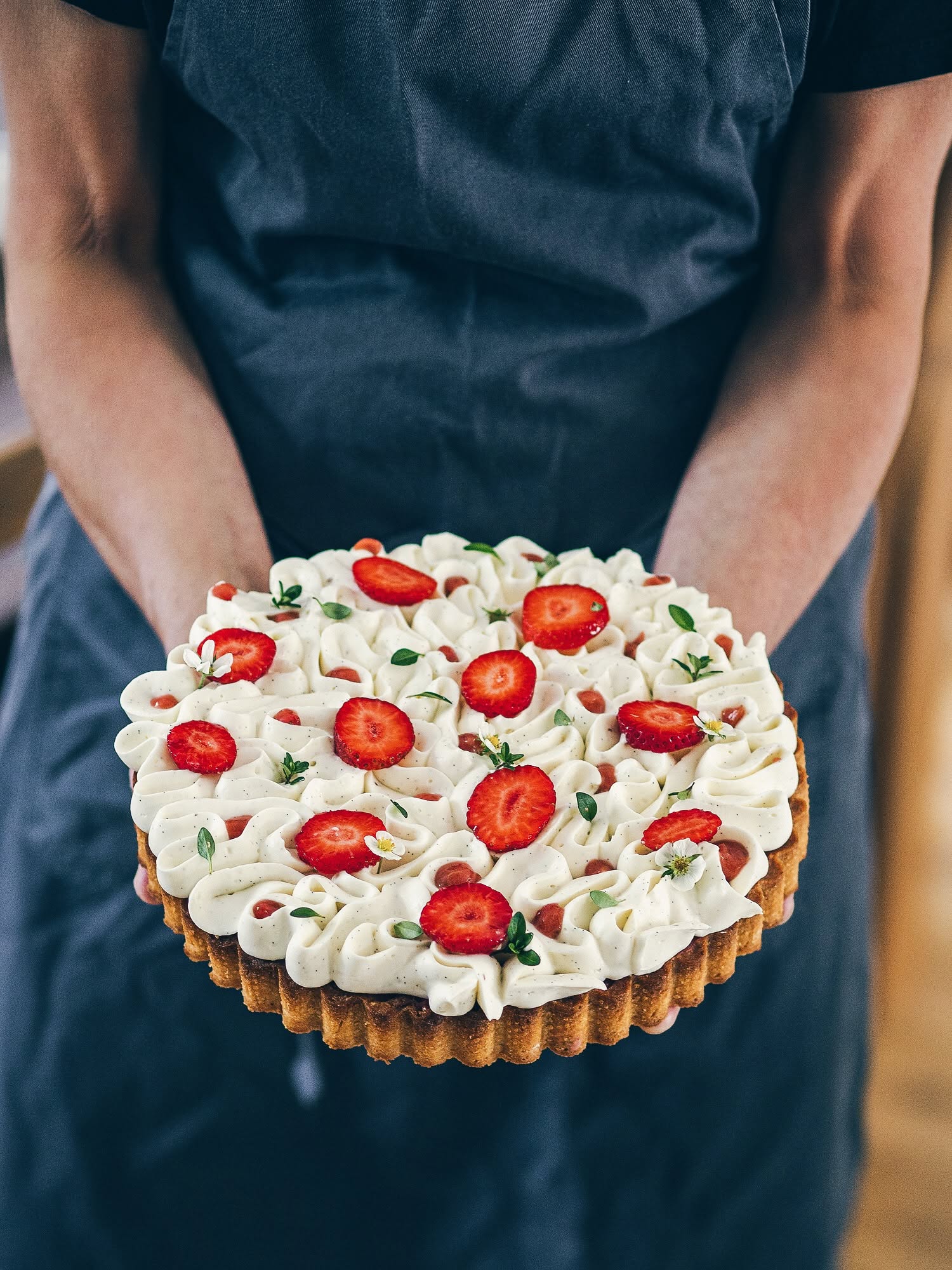 Žena v zástěře drží upečený jahodový tart s vanilkou ozdobený jahodami